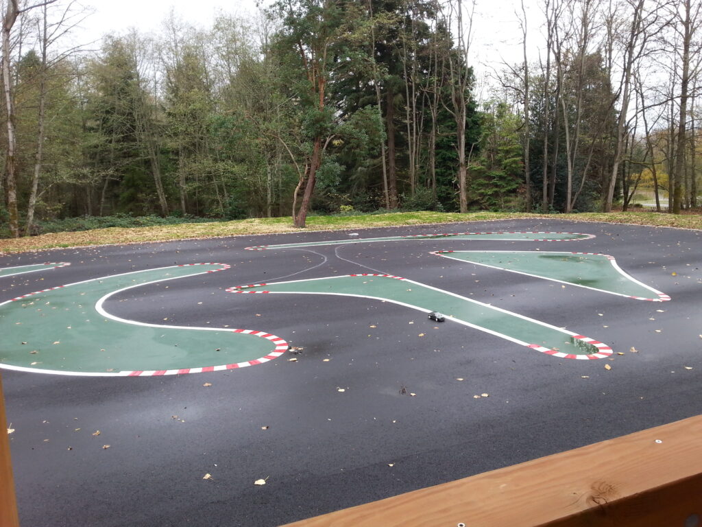 On-road RC track made out of black asphalt. It has green spaces lined with red and white borders to create different routes. 