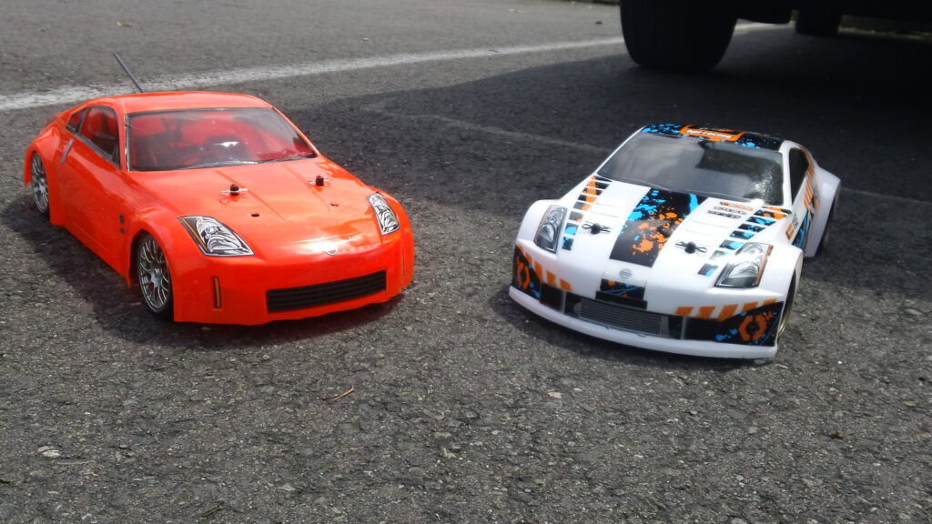 Two 350Z RC cars side by side. One orange and one white with blue and orange accents. 