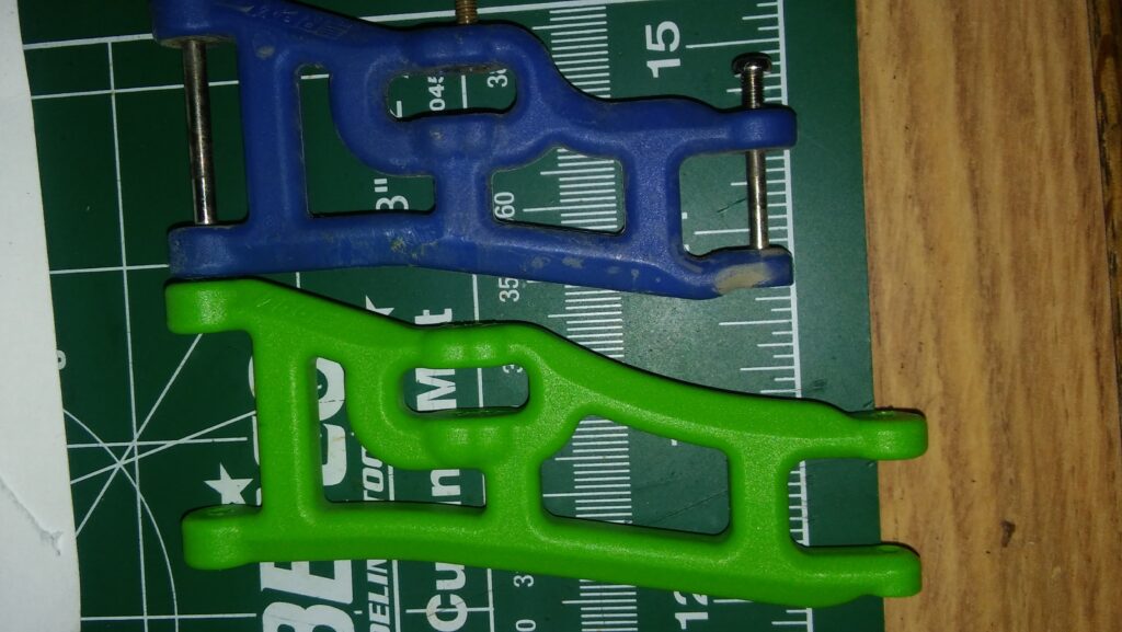 One green wide RPM A-arm sitting next to one blue standard A-arm 