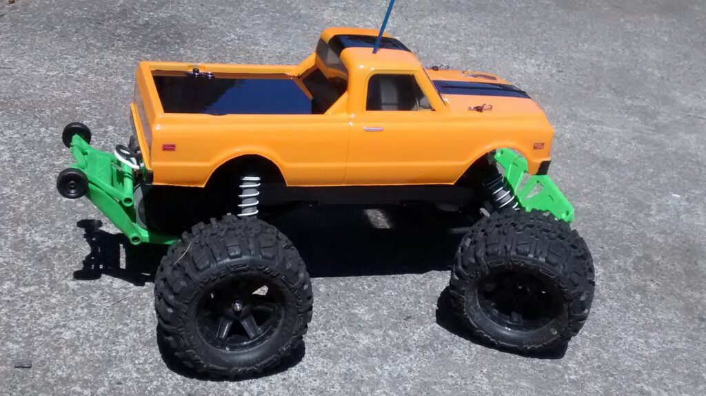 Side profile of a light orange and black Traxxas Stampede RC monster truck with a green wheelie bar