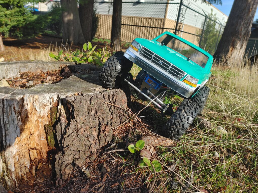 Green and white RC truck crawling over a stump