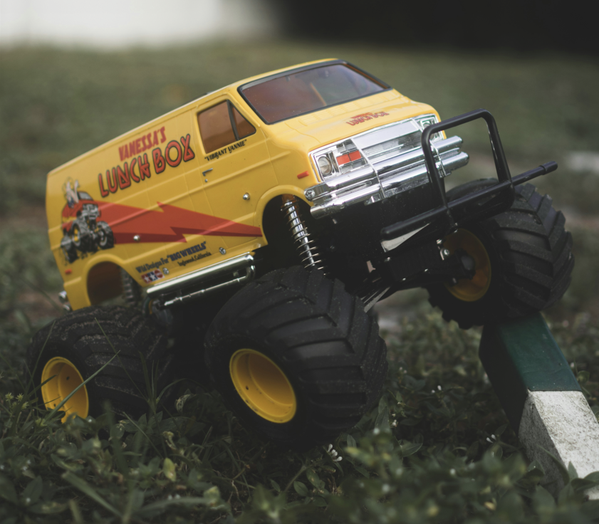 A photo of the original Tamiya Lunchbox depicts a bright yellow 1/12 scale RC van with a bold, retro design. The van features oversized, deep-tread tires, giving it a rugged, monster truck-like appearance.